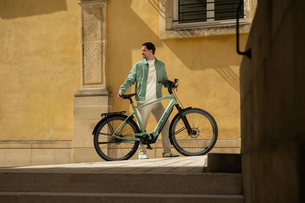 man standing next to a cortina e-silento shole green men's bike